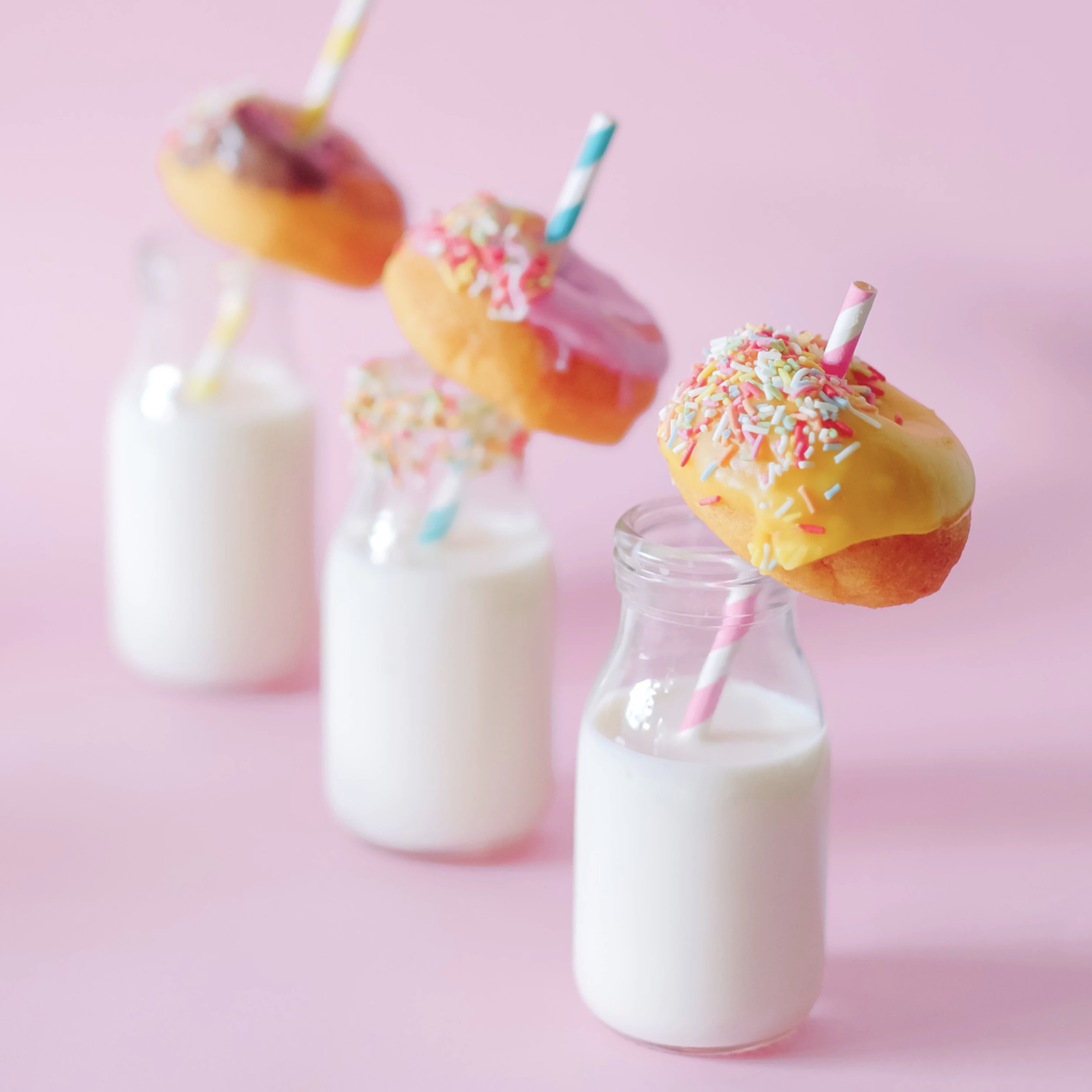 Three glasses of milk with straws and donuts with sparkles.