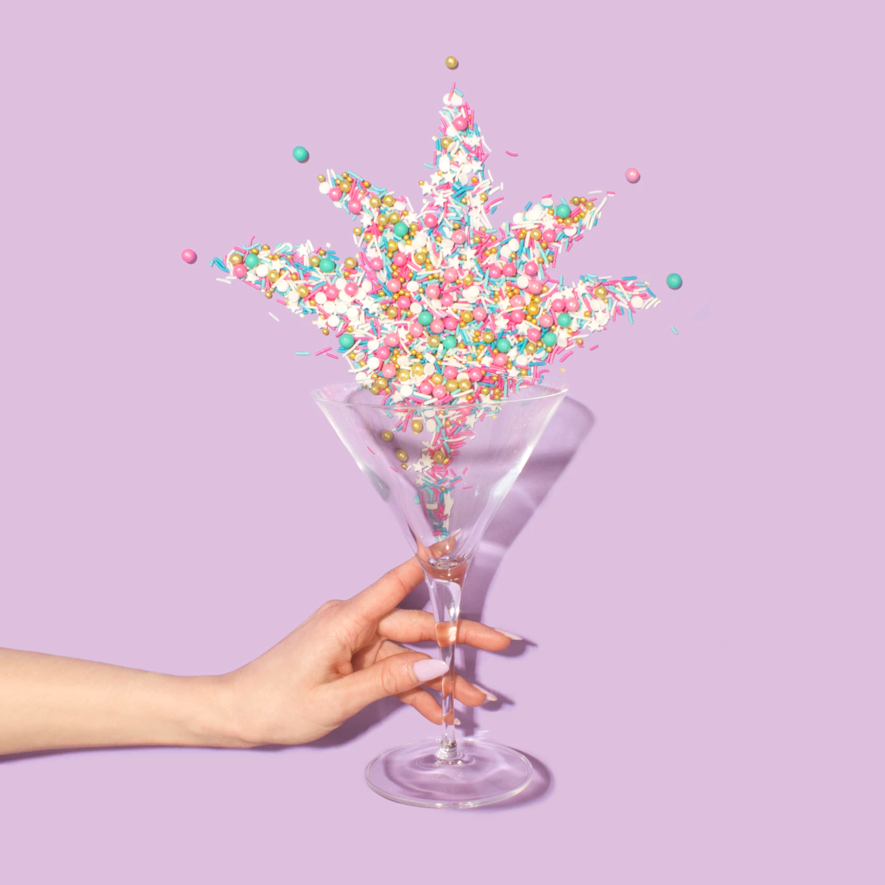 A held glass spilling sprinkles on a lilac background.